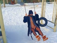 Nude tomboy in a fur coat swings on a swing in winter