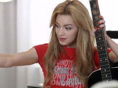 An anal loving redhead is on the bed, playing with a guitar